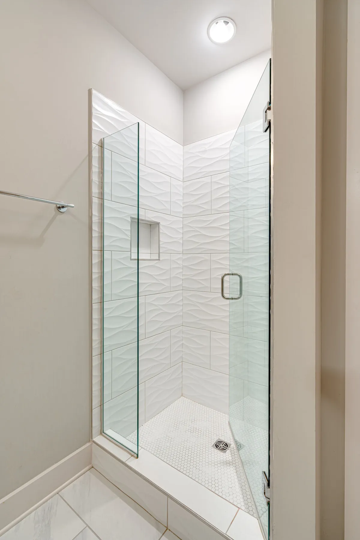 A modern bathroom with a glass shower enclosure, textured wall tiles, and hexagonal floor tiles. The mood is serene and spa-like, suggesting a luxurious and rejuvenating space for self-care routines and relaxation after a long day.