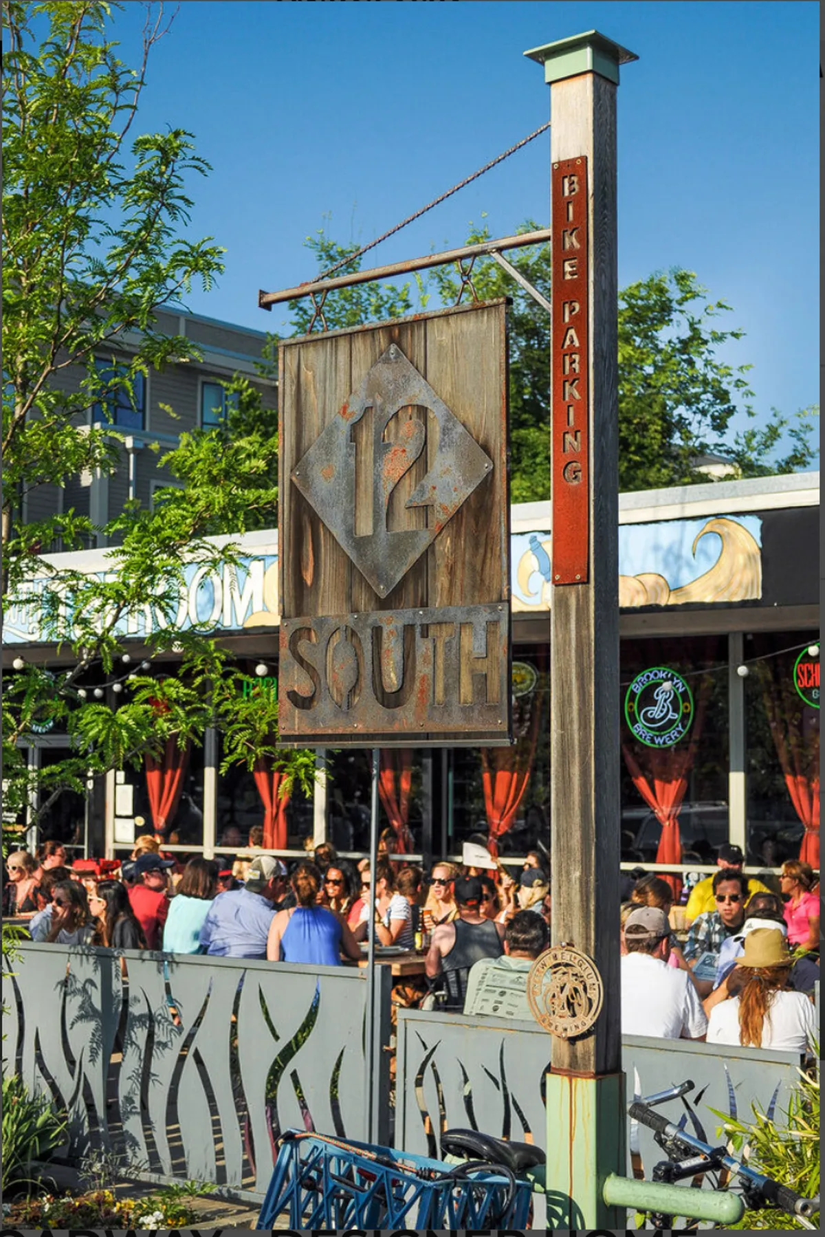 A lively exterior of a local venue with signage, outdoor seating, and people dining. The decorative fence and illuminated atmosphere suggest a hotspot for live music nights, socializing, and enjoying local culture.