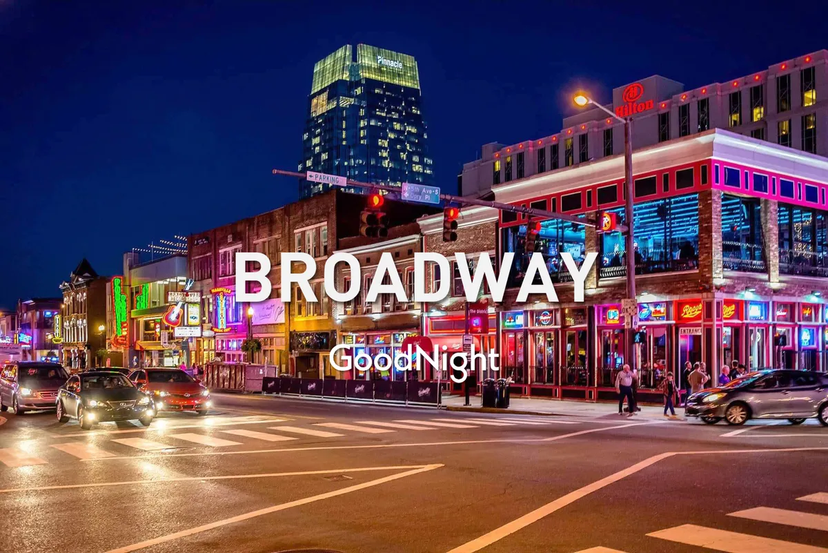 A vibrant nighttime street scene featuring bright neon signs, bustling sidewalks, people walking, and cars passing by. The energy of the nightlife is palpable, with restaurants, bars, and venues lining the street, immersing viewers in Nashville's electric after-dark atmosphere.