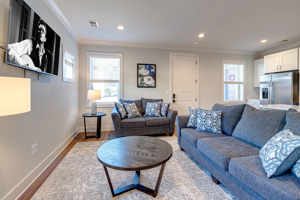 A spacious living room with a large gray sectional sofa, a round wooden coffee table, wall art, and a television. The atmosphere is comfortable and welcoming, encouraging relaxation, movie nights, and gatherings with friends or family.